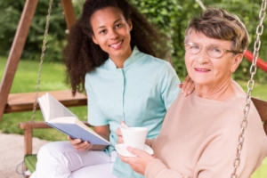 elderly woman holding a cup of coffee with her caregiver holding a book